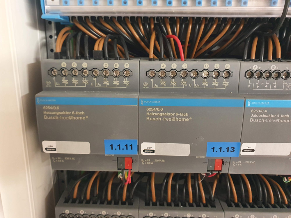 Drei graue Heizungsaktoren mit blauen Aufklebern und zahlreichen Kabeln davor