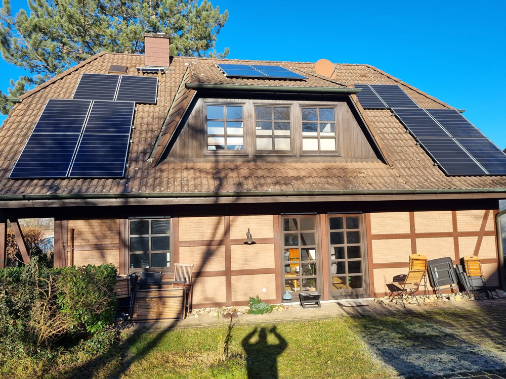 Ein Haus mit braunem Ziegeldach und mehreren schwarzen Solarmodulen in der Sonne