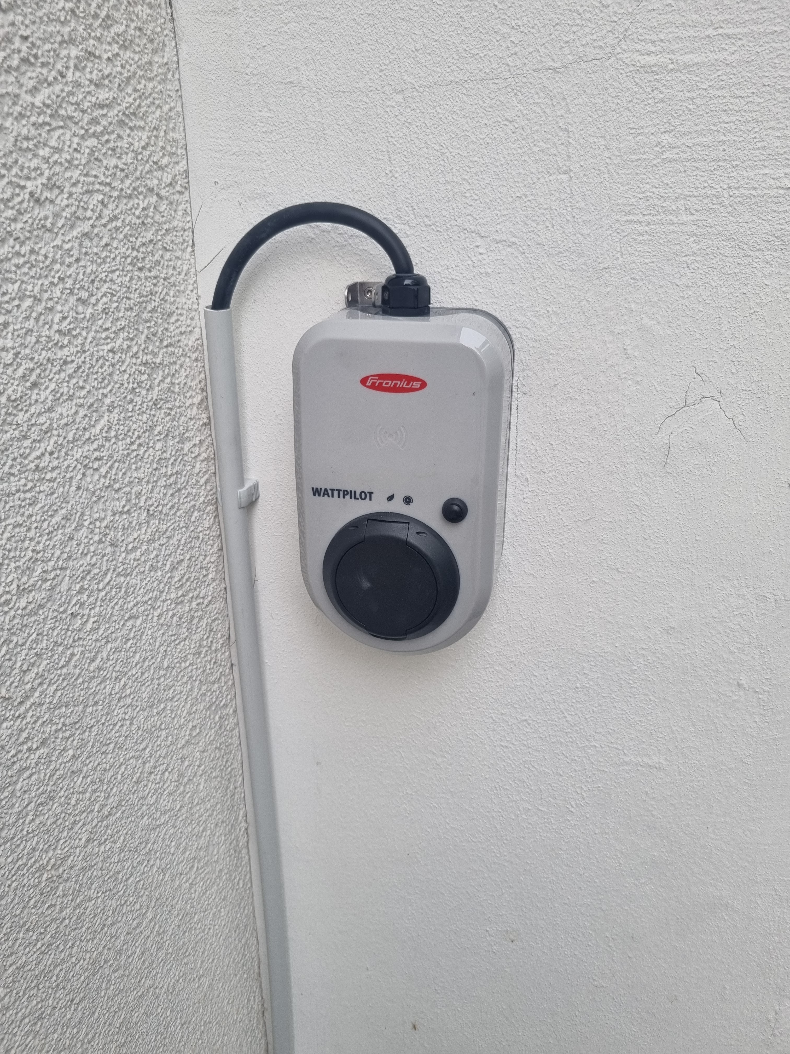 Eine graue Ladestation mit schwarzem Anschlusskabel ist an einer weißen Wand montiert