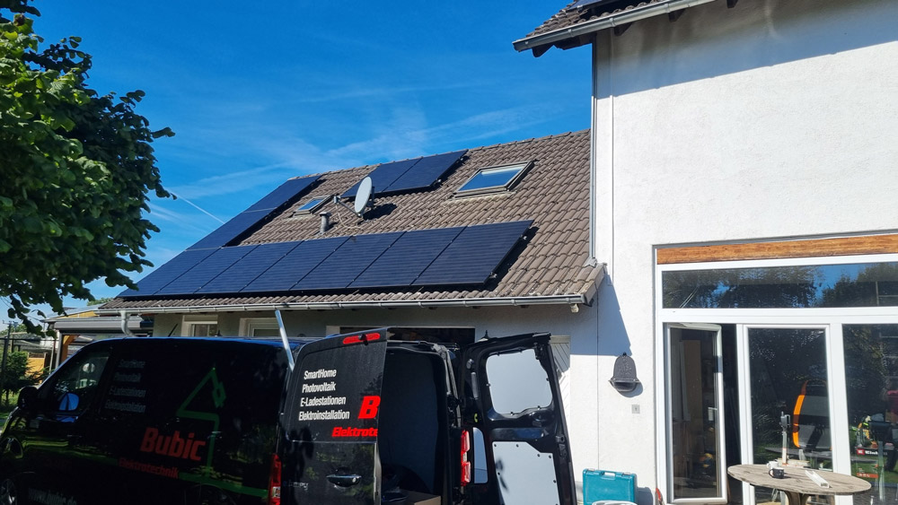 Ein weißes Haus mit dunklen Solarmodulen auf dem Dach bei sonnigem Wetter