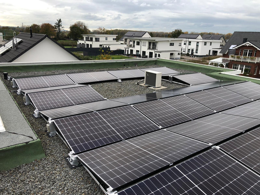 Eine flache Dachfläche mit vielen schwarzen Solarpanelen und einigen modernen Häusern im Hintergrund
