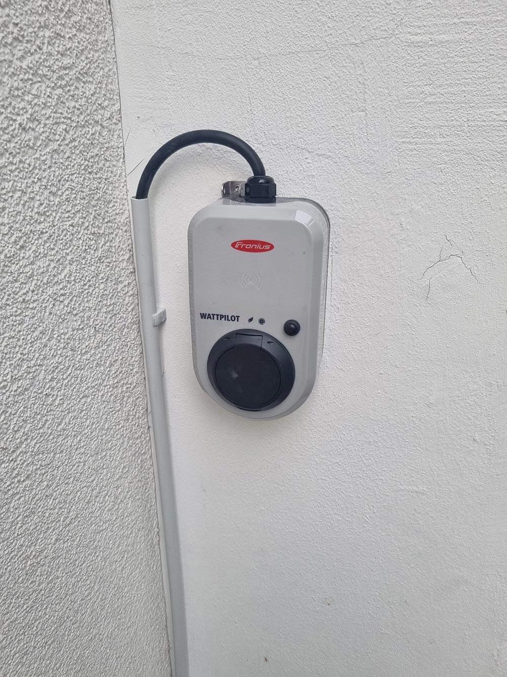 Graue Wallbox mit schwarzem Drehregler und Kabel an weisser Wand