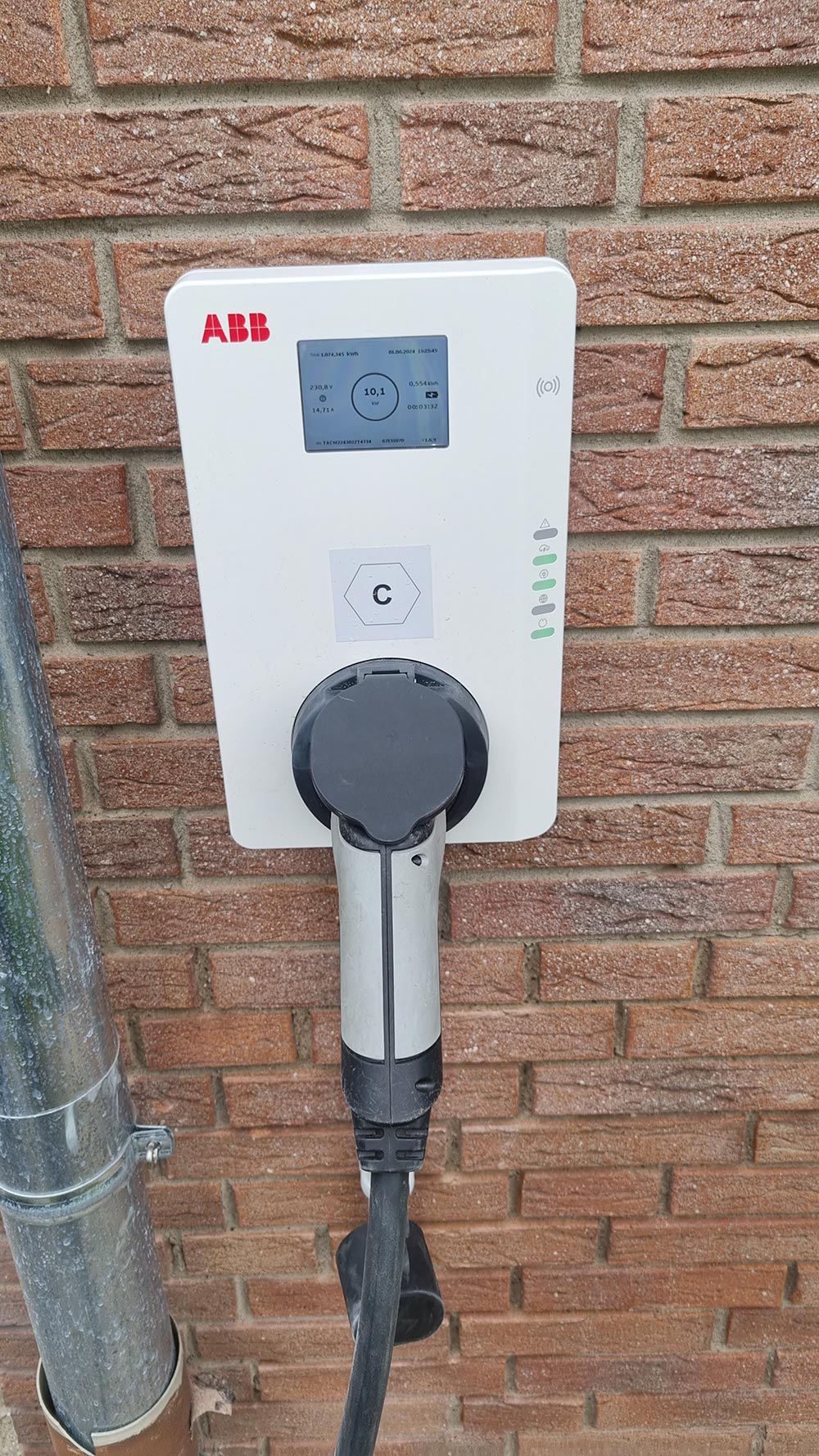Weisse ABB Wallbox mit Display und schwarzem Stecker vor roter Ziegelwand